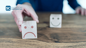 A Person Holding a Block With An Unhappy Face Ahead of a Block With a Happy Face and a Shoppers Confidential Logo